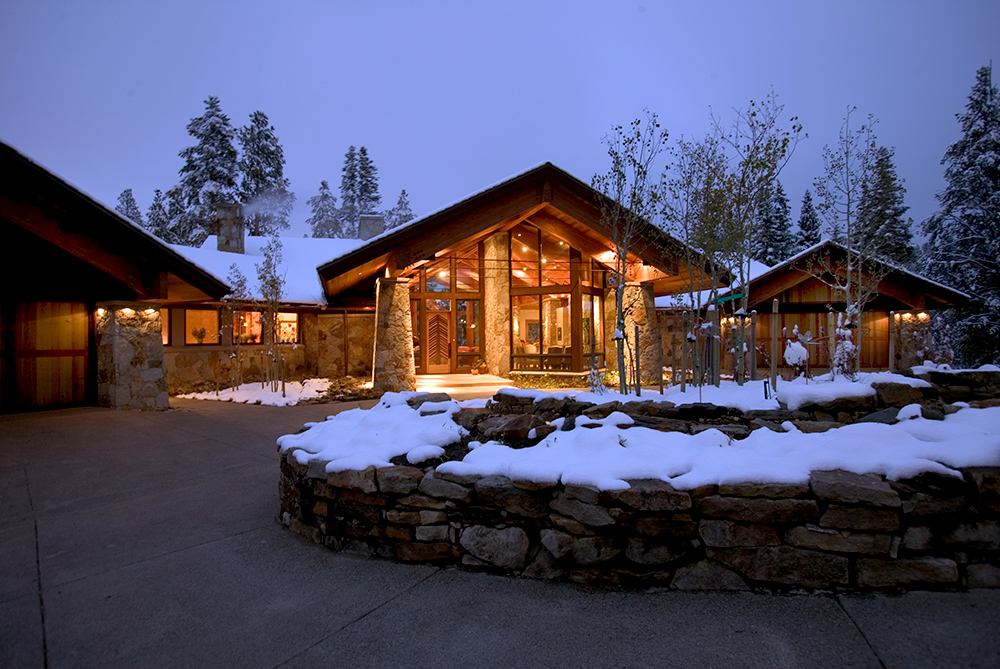 front view of a custom home in a mountain setting, well lite entry, snow in front.