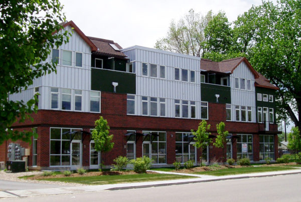 contemporary multi-use building with vertical aluminum siding and a red brick exterior on the first floor of the three levels