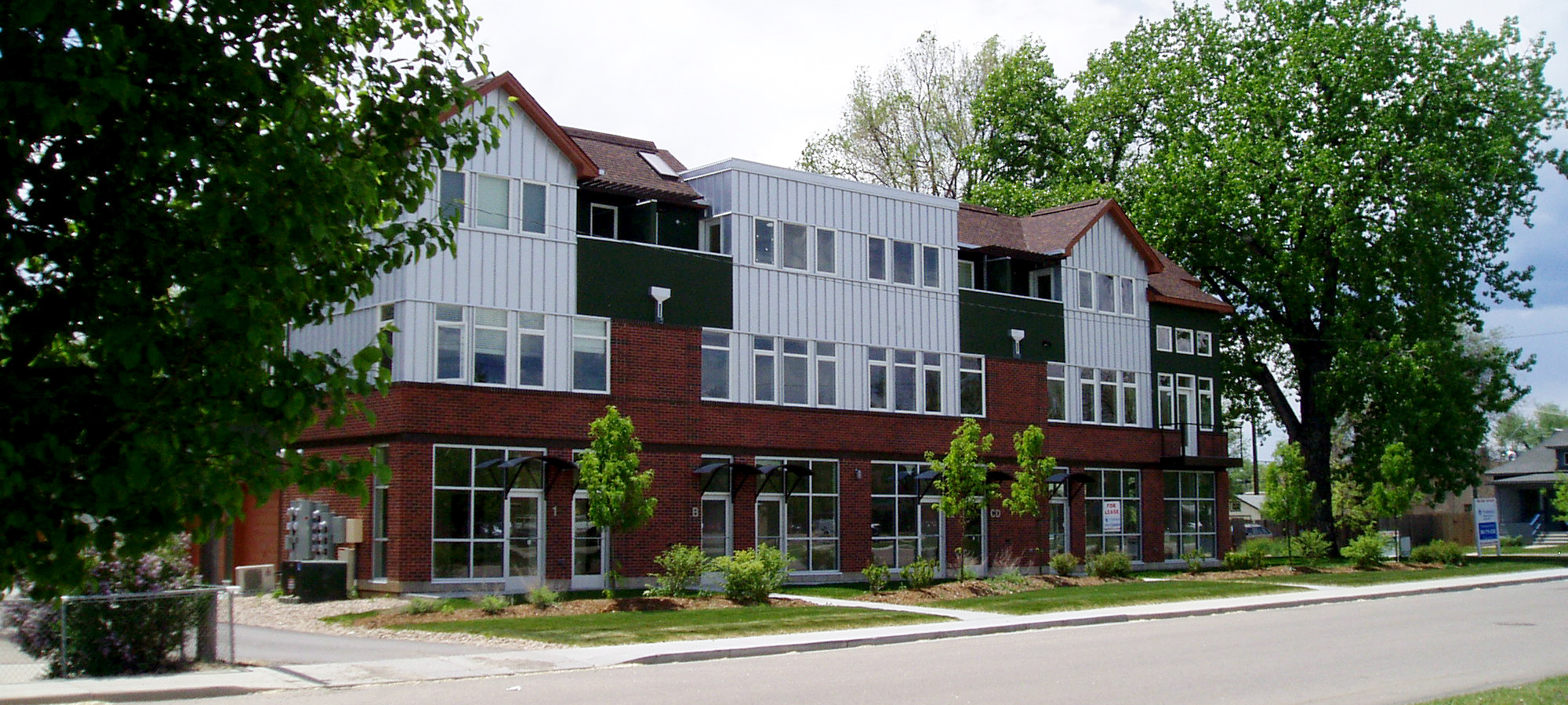 contemporary multi-use building with vertical aluminum siding and a red brick exterior on the first floor of the three levels